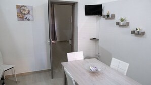 A dining area with a wooden table, white chairs, a door, and a wall-mounted TV. - A stone's throw from downtown and the sea modern comfort and the scent of Marsala bread (Marsala)