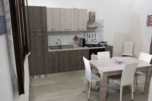 A modern kitchen with grey cabinets, a stainless steel sink, and a dining area with a white table and chairs. - A stone's throw from downtown and the sea modern comfort and the scent of Marsala bread (Marsala)