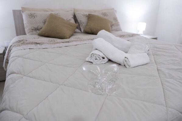 A neatly made bed with a quilted white duvet, two brown pillows, and a folded white towel on the bed.