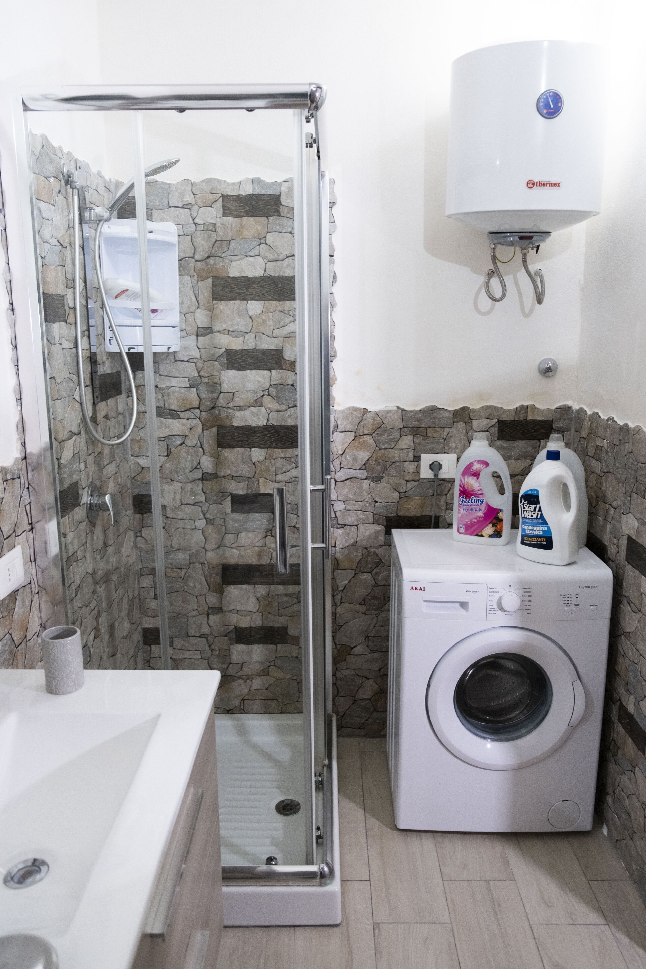 Un baño con ducha de vidrio, lavadora y calentador de agua.