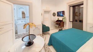 A hotel room with a bed, a desk with a computer, a chair, a small table with a decorative item, and a mirror. - Moresco (Catania)