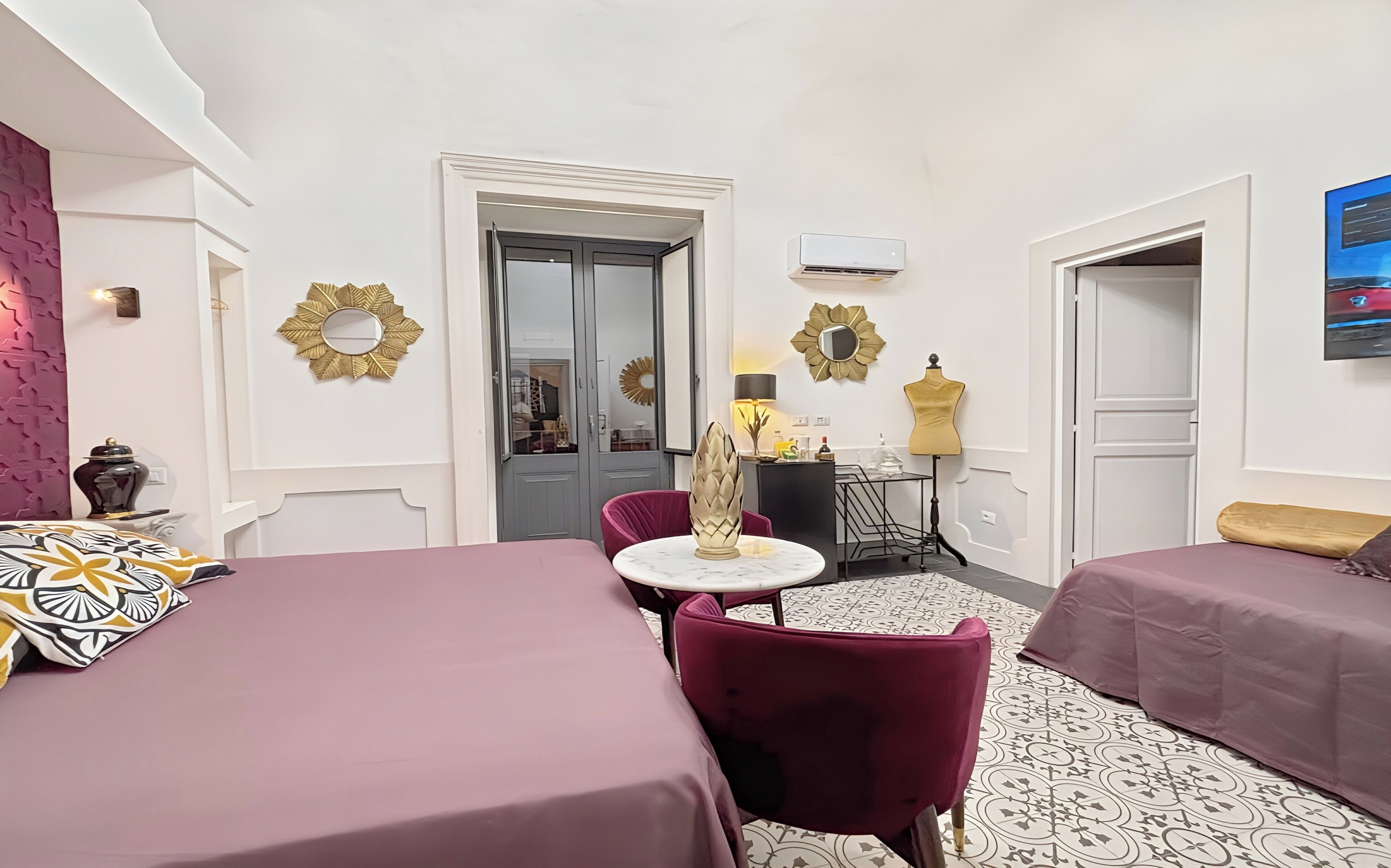 A hotel room with two beds, a small table with a lamp, decorative wall mirrors, and a mannequin.