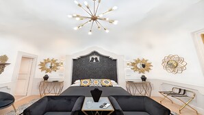 A modern bedroom with a large bed, a chandelier, decorative wall mirrors, and a small side table. - Moresco (Catania)