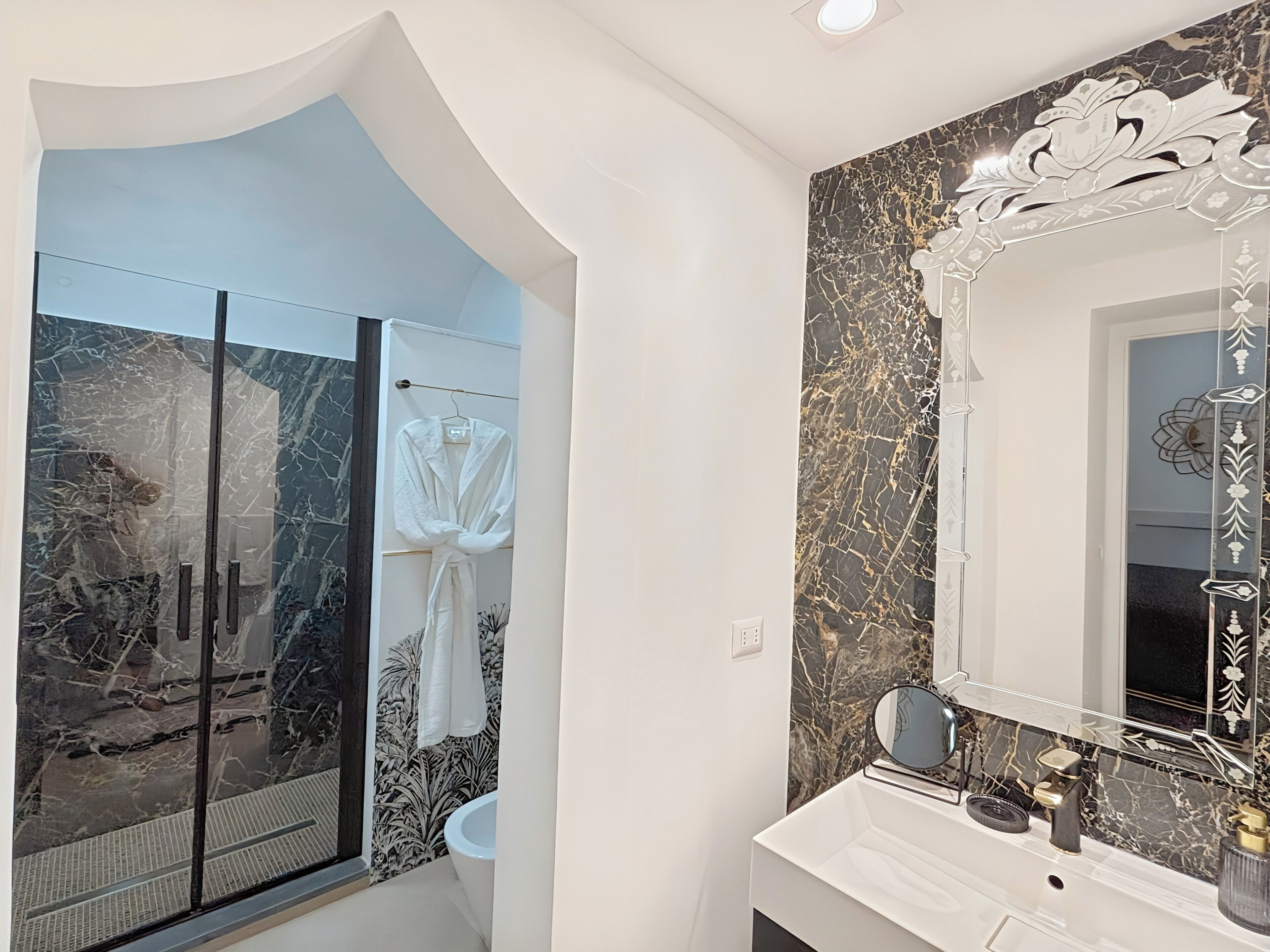Un baño moderno con salpicadero de mármol, un espejo grande y mampara de ducha de vidrio.