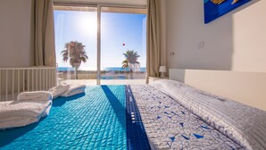 Ein Hotelzimmer mit einem großen Bett, Blick auf Palmen und das Meer sowie einem Bild an der Wand.