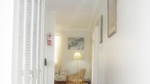 A hallway leading to a bedroom with a bed, a chair, a lamp, and a painting on the wall. - Seabreeze Villa: Best rates. Charming, bright & spacious. Truly a home from home (Atlantic Shores)