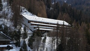 Un edificio imbiancato dalla neve con numerosi balconi, circondato da alberi e montagne.