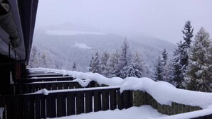 Un pontile in legno con accumulo di neve, con vista su una catena montuosa ricoperta di alberi.