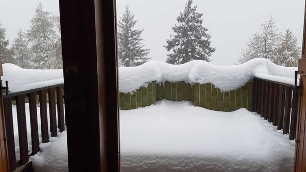 Un balcone innevato con ringhiera in legno e vista su alberi coperti di neve.