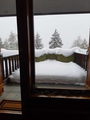 Un balcon enneigé, doté d’une balustrade en bois, d’où l’on peut admirer des arbres recouverts de neige.