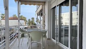 A balcony with a table and chairs, a sliding glass door, and a view of palm trees and buildings. - Alexis plus Zeus Salou  3121 (Salou)