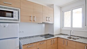 A kitchen with wooden cabinets, a built-in microwave, a stainless steel sink, and a granite countertop. - Alexis plus Zeus Salou  3121 (Salou)