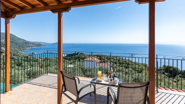 Eine Terrasse mit gedecktem Tisch für zwei Personen, mit Blick auf eine Küstenlandschaft, in der Meer und Hügel klar zu sehen sind.