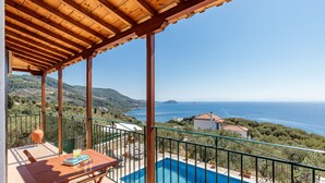 Eine Holzterrasse mit Pool, Gartenmöbeln und Blick aufs Meer.