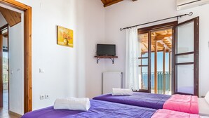Ein Schlafzimmer mit zwei Betten, einem Fernseher auf einem Regal, einem Gemälde und Blick ins Freie.