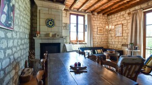 A rustic room with a stone wall, wooden ceiling beams, a fireplace, a dining table, and a sofa. - Loire Valley with pool (Thizay)
