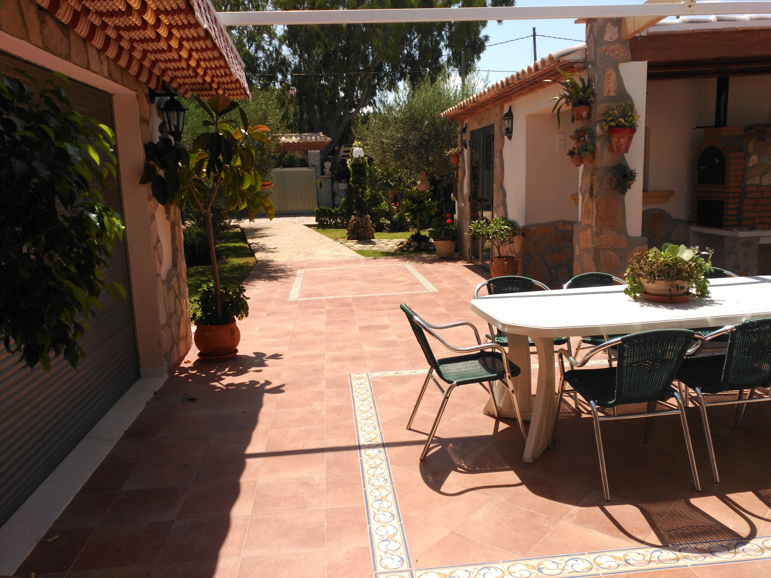 Eine Terrasse mit Tisch und Stühlen, umgeben von Kübelpflanzen und einer Steinmauer.
