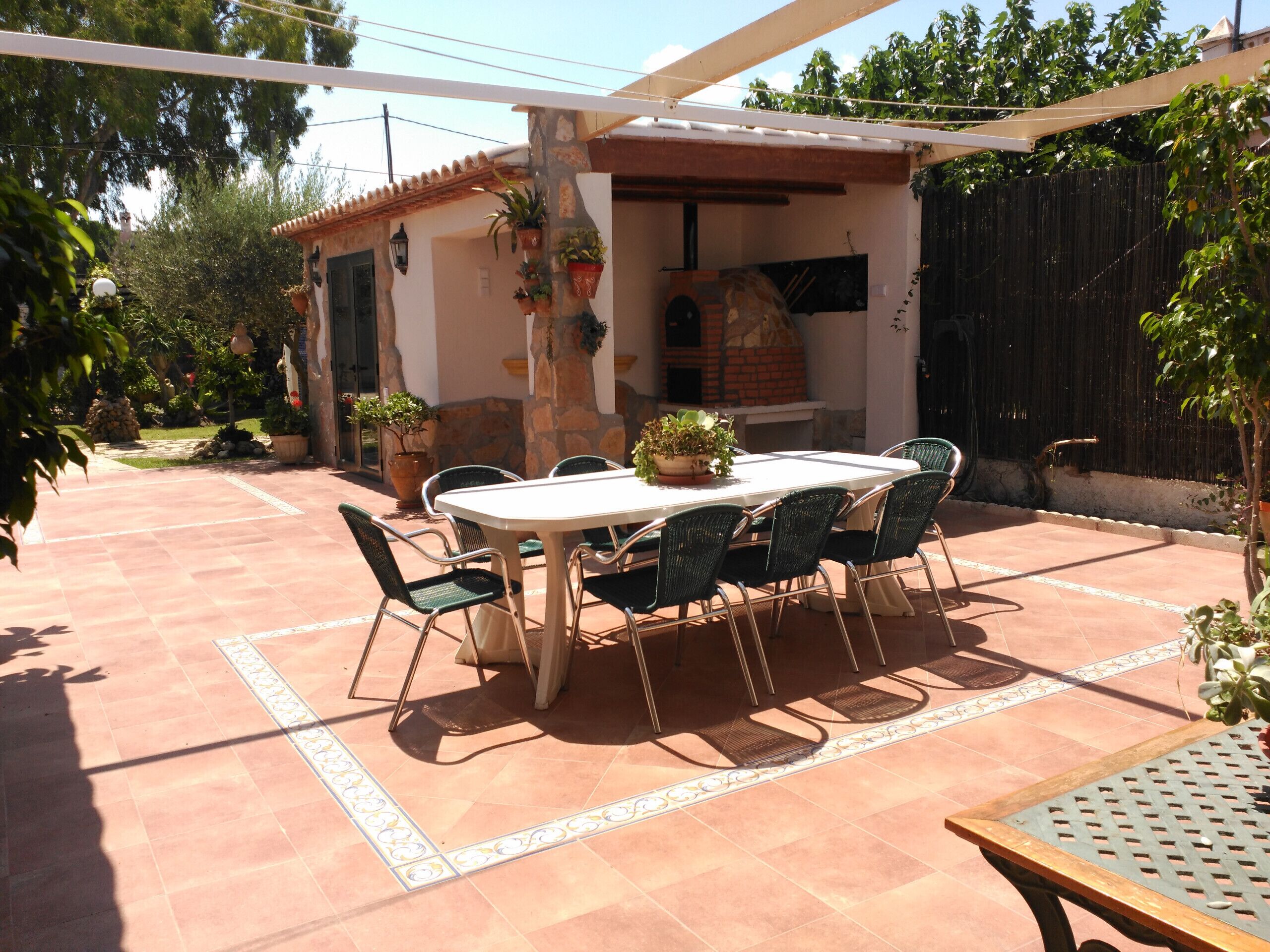 Un patio al aire libre con una mesa redonda y sillas, un horno de ladrillo y plantas en macetas.