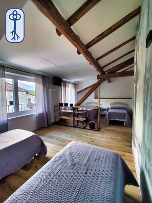 A room with a sloped ceiling, wooden beams, two beds, a desk, and a window with a view.