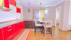 Une cuisine moderne avec des meubles de rangement rouges, un plan de travail en granit et un coin repas comprenant une table et des chaises.