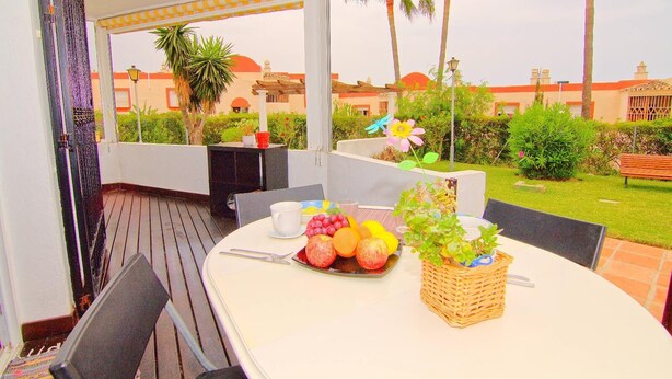 Une terrasse extérieure avec une table dressée pour le repas, entourée de verdure et de palmiers.