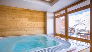A wooden-paneled room with a hot tub and a large window overlooking a snowy mountain.