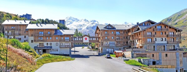 Ein Bergresort mit Holzbauten, einer Straße, die zum Eingang führt, und einer Aussicht auf schneebedeckte Berge im Hintergrund.