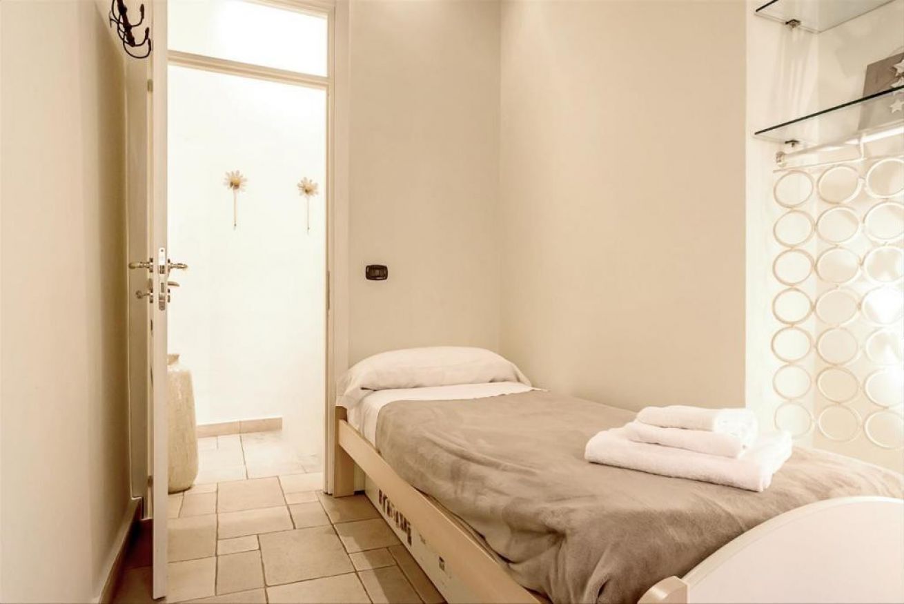 A small, clean bedroom with a bed, a door leading to a bathroom, and a shower area.