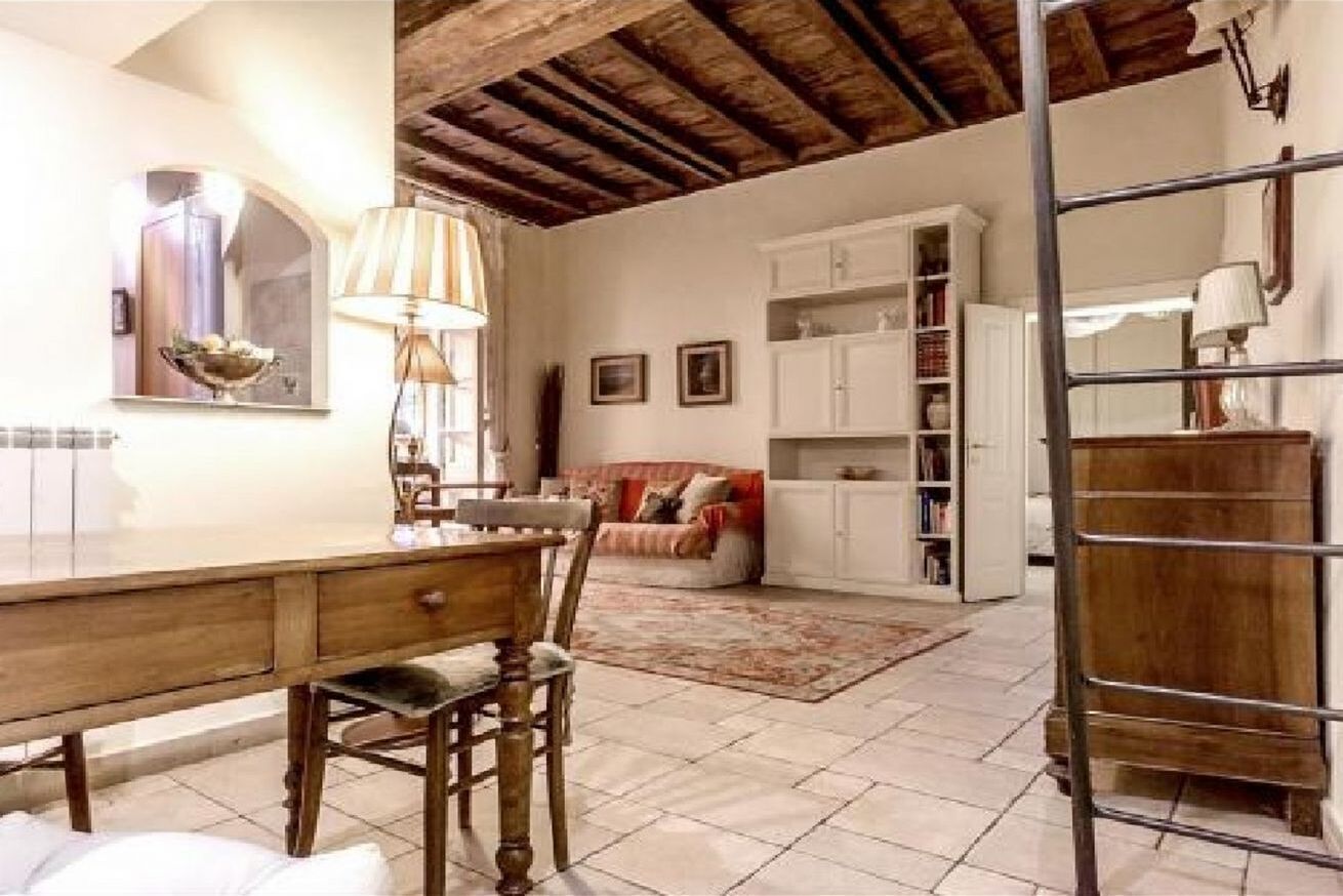 A room with a wooden dining table, chairs, a sofa, a bookshelf, and a ladder.