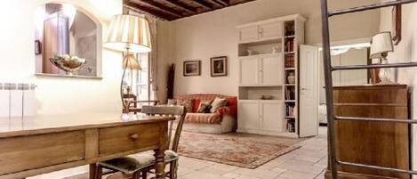 A room with a wooden dining table, chairs, a sofa, a bookshelf, and a ladder.