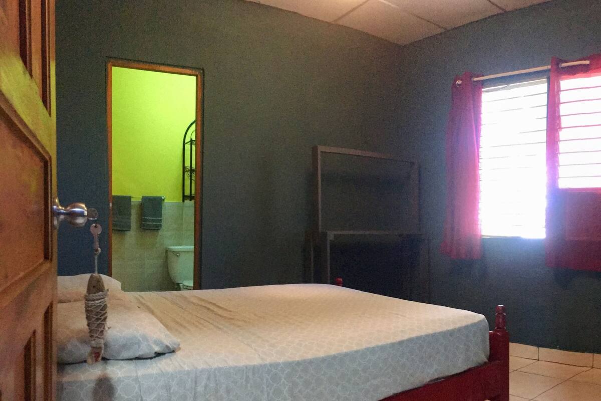 A room with a bed, a door, a window with curtains, and a mirror.