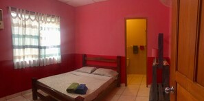 A room with a bed, a wooden headboard, a window with curtains, a door, and a small table with a lamp. - Residencia de la Marina (Boca Chica)