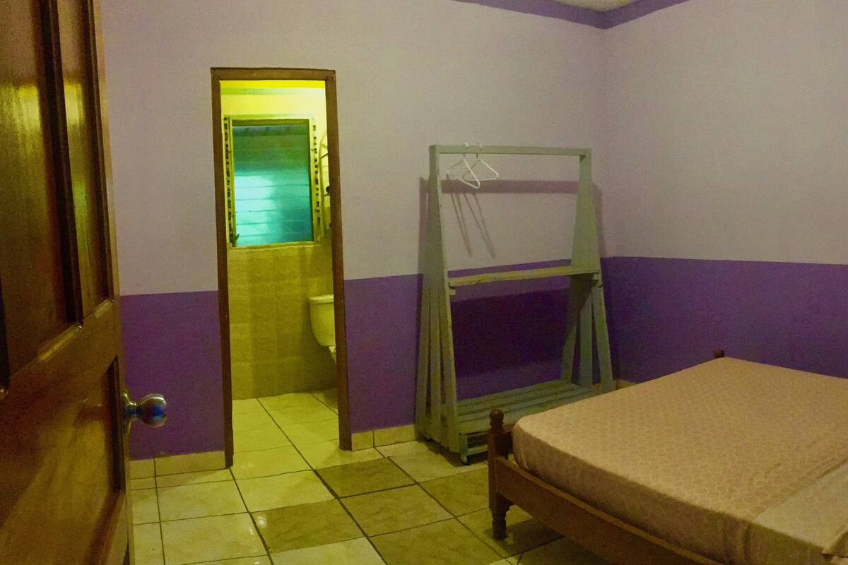 A room with a bed, a wooden door, a mirror, and a window.