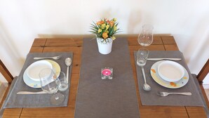 Ein Esszimmertisch ist gedeckt mit Tellern, Schüsseln, Besteck und Gläsern, in der Mitte steht eine Blumenvase und eine Kerze.