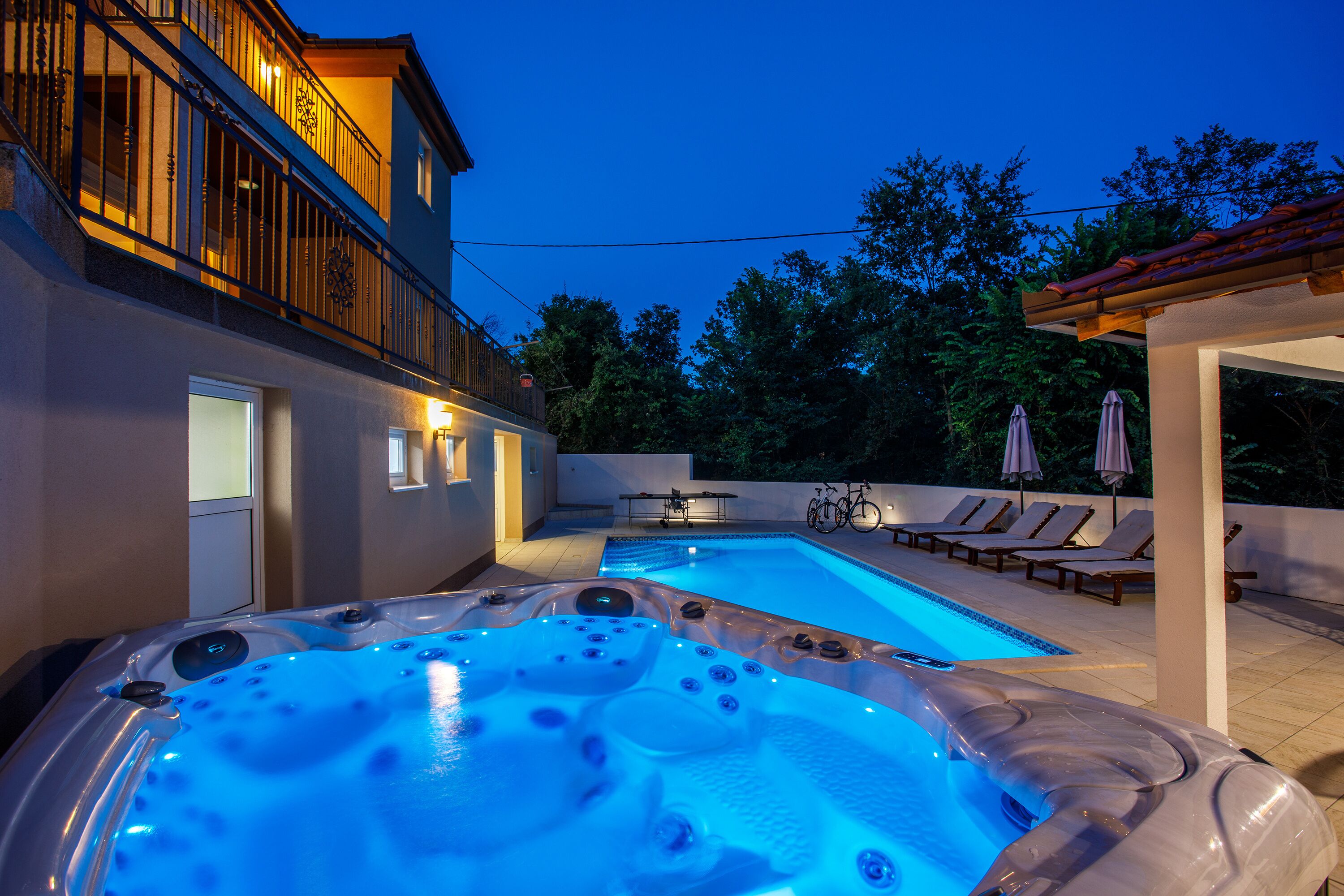 Ein Swimmingpool mit Whirlpools, Liegestühlen und einem überdachten Bereich mit Sonnenschirmen.