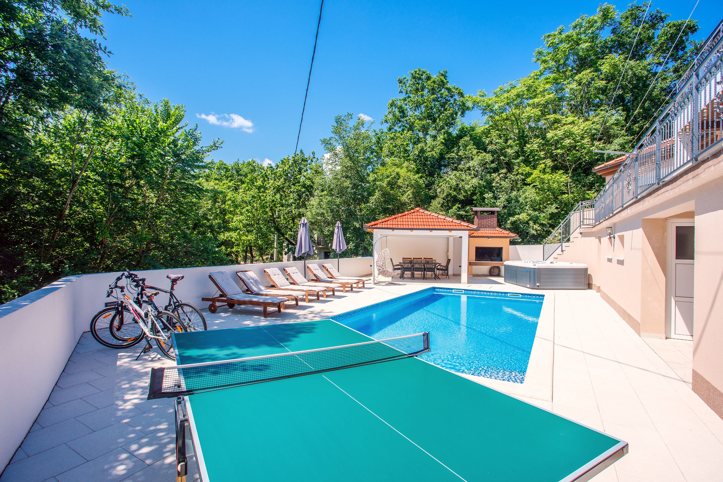 A swimming pool with a sun terrace, lounge chairs, and a covered seating area.