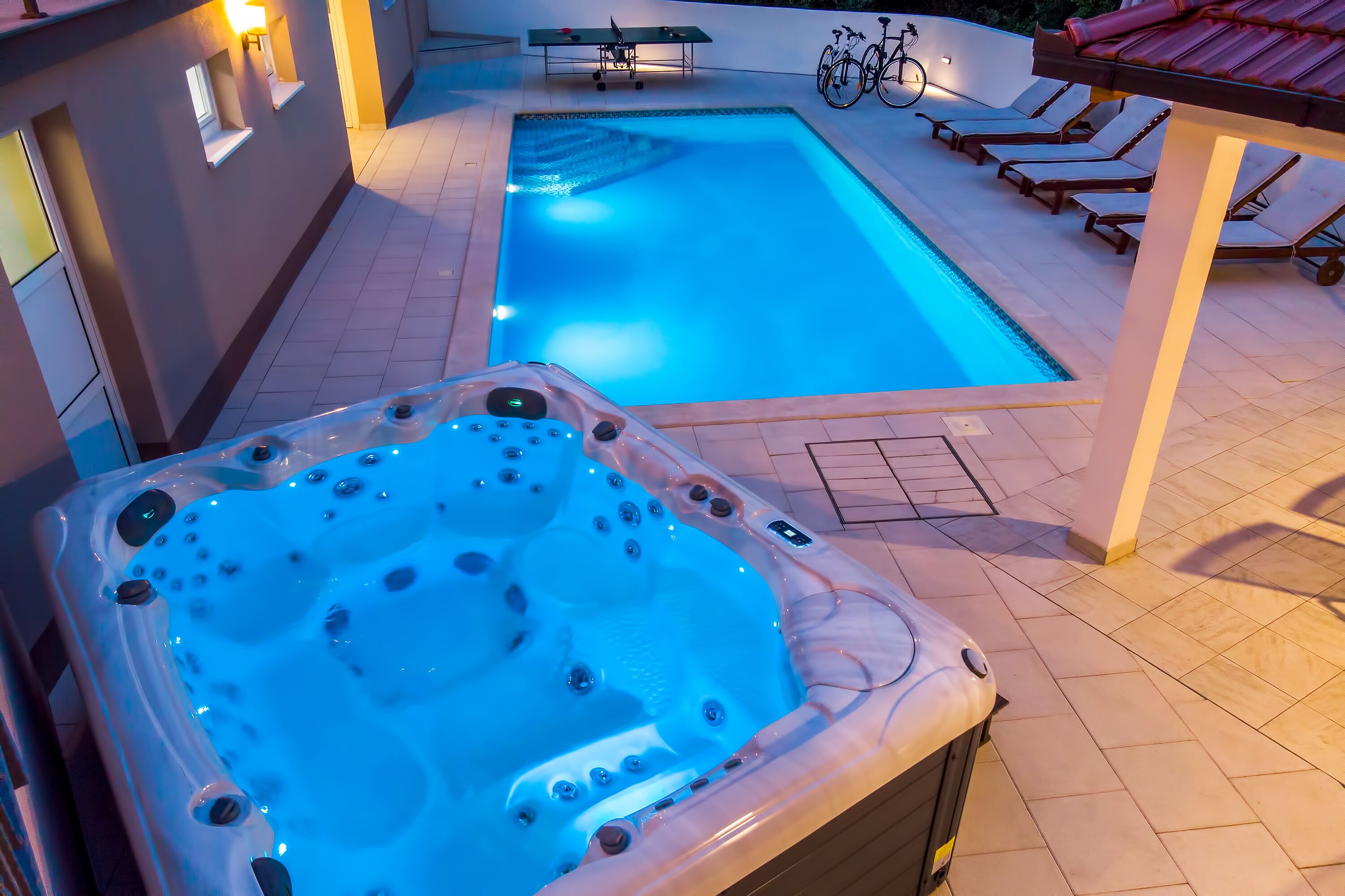 Een zwembad met ligbedden en een jacuzzi.