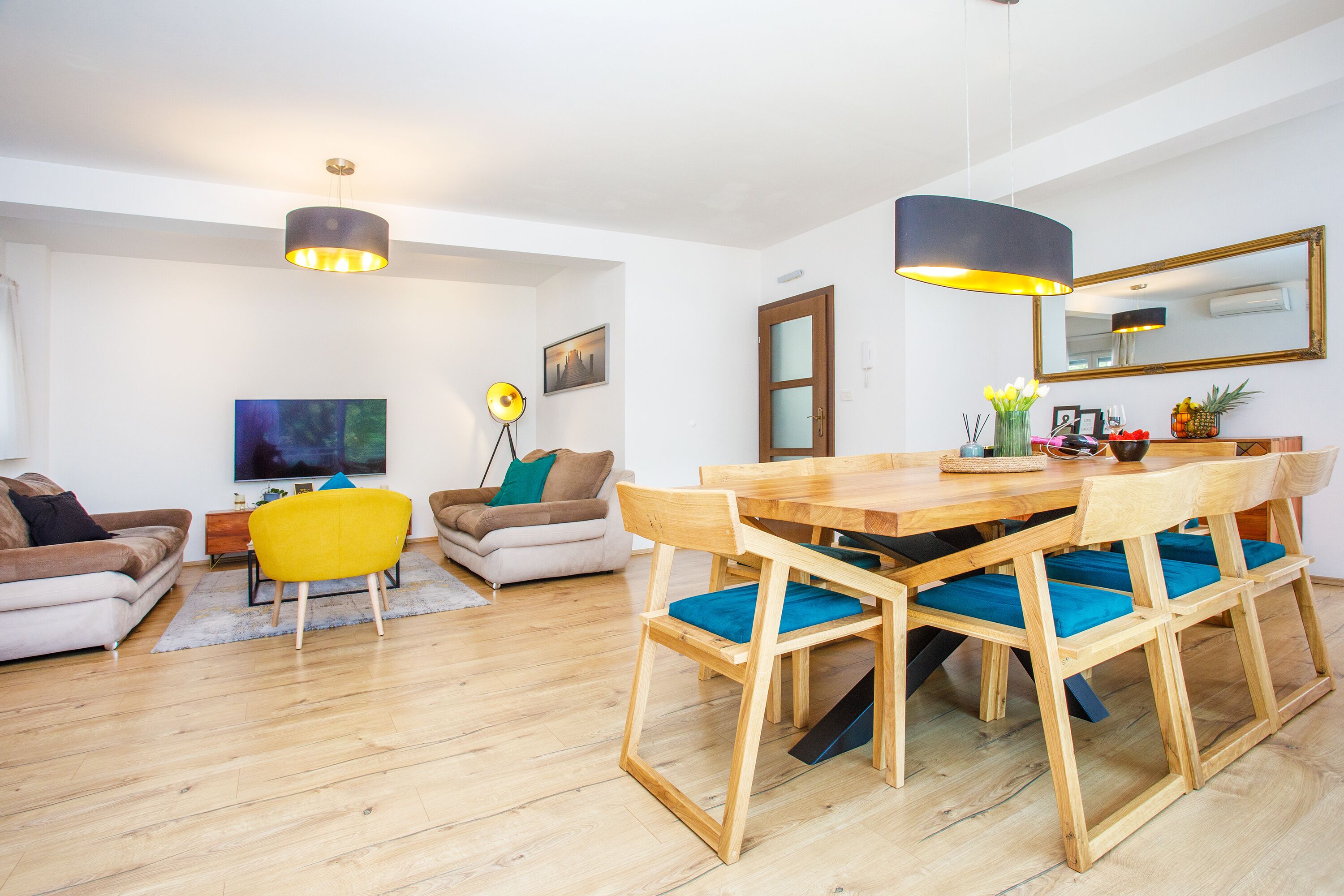 Un salon moderne avec une table à manger en bois, des chaises rembourrées bleues, un fauteuil jaune et un grand téléviseur à écran plat.
