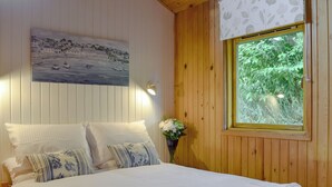 A bedroom with a bed, pillows, a painting, a window, and a vase with flowers.