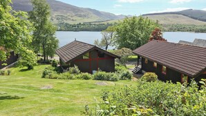 A lakeside property with two buildings, a grassy lawn, and a mountain backdrop.