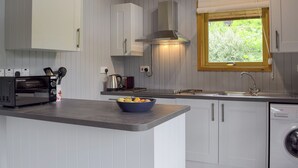 A kitchen with white cabinets, a toaster, a kettle, a sink, and a window with a view of greenery.