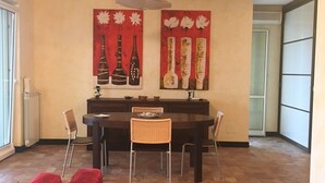 A dining area with a table and chairs, a red couch, and a wall with two paintings of vases. - apartment on the sea (Badolato Marina)