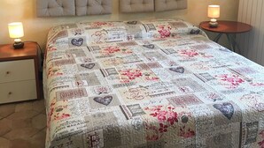 A bedroom with a quilted bedspread featuring vintage-style designs, a bedside table with a lamp, and a radiator on the wall. - apartment on the sea (Badolato Marina)