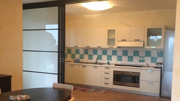 A modern kitchen with white cabinets, a tiled backsplash, and a dining area with a table and chairs. - apartment on the sea (Badolato Marina)