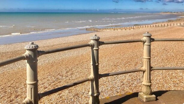 A pebble beach with a metal railing and a clear view of the ocean.
