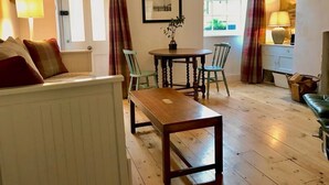 A cozy living room with a wooden table and chairs, a white radiator, a door, and a window with curtains.