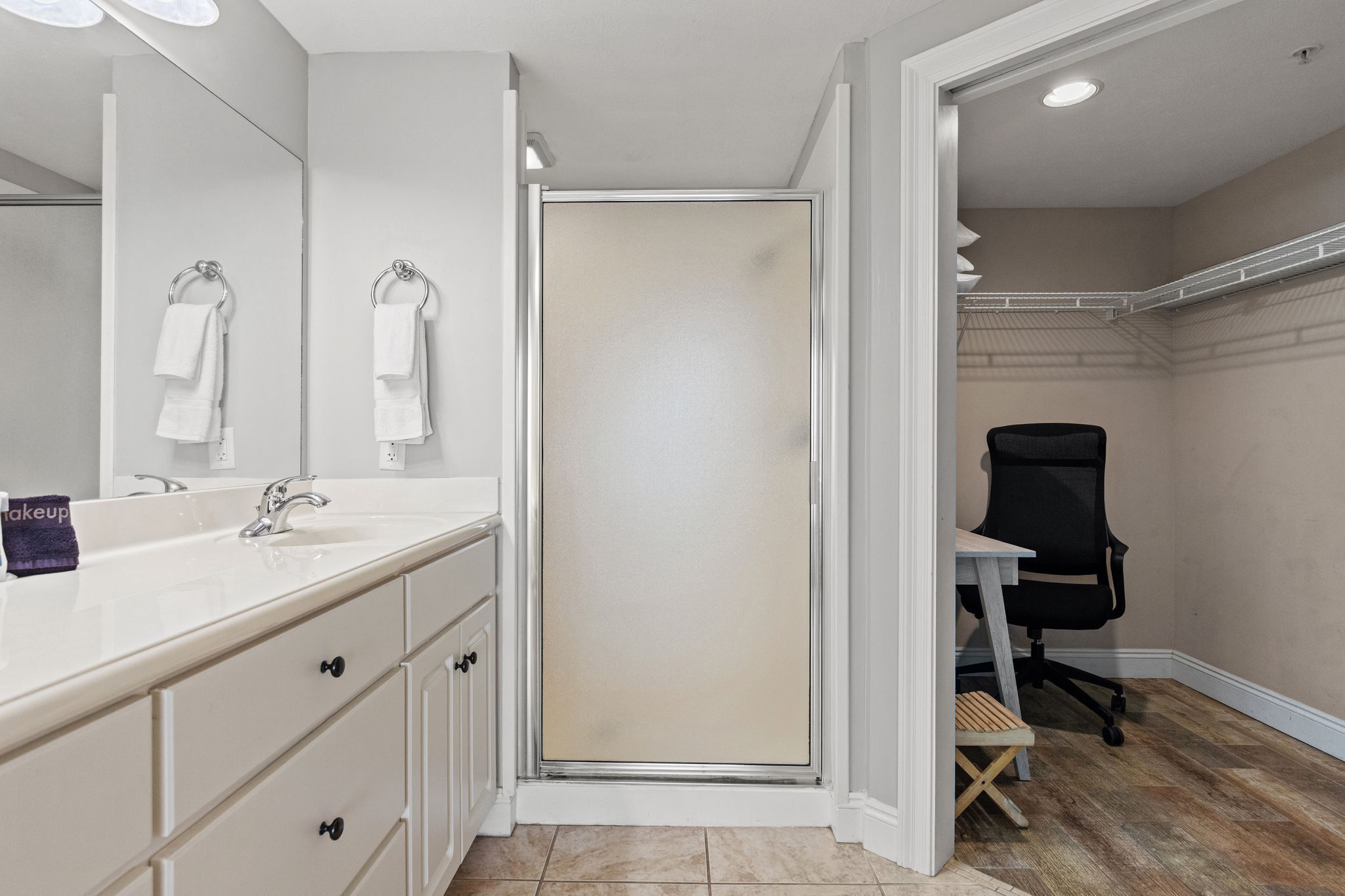 Un baño con tocador blanco, cabina de ducha y una silla de oficina negra.