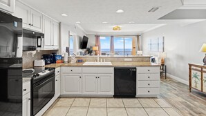 Una cocina moderna con armarios blancos, un refrigerador de acero inoxidable, horno empotrado, lavavajillas y una isla grande con pileta.