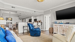 Un salón amplio con un sofá, un sillón reclinable, un televisor de pantalla plana y una cocina al fondo.