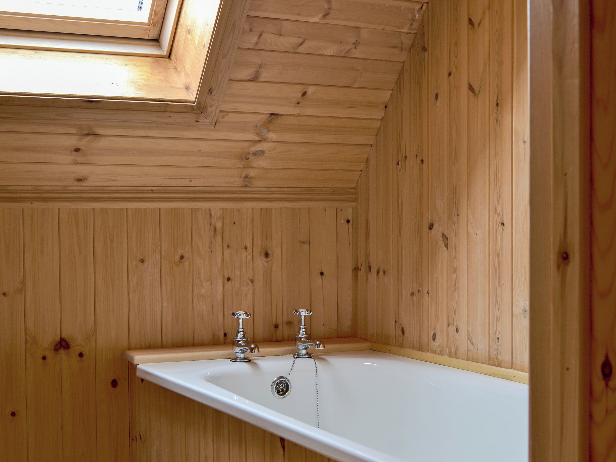 A wooden-paneled bathroom with a bathtub and two faucets.